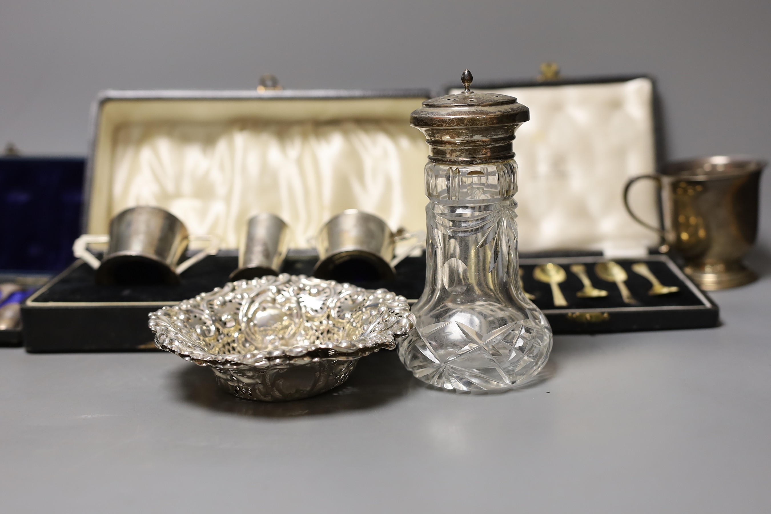 A group of mixed silver, including a cigarette box, two silver christening mugs, two similar pierced bonbon dishes, a cased Art Deco three piece condiment set, two cased sets of six teaspoons one enamelled stamped sterli